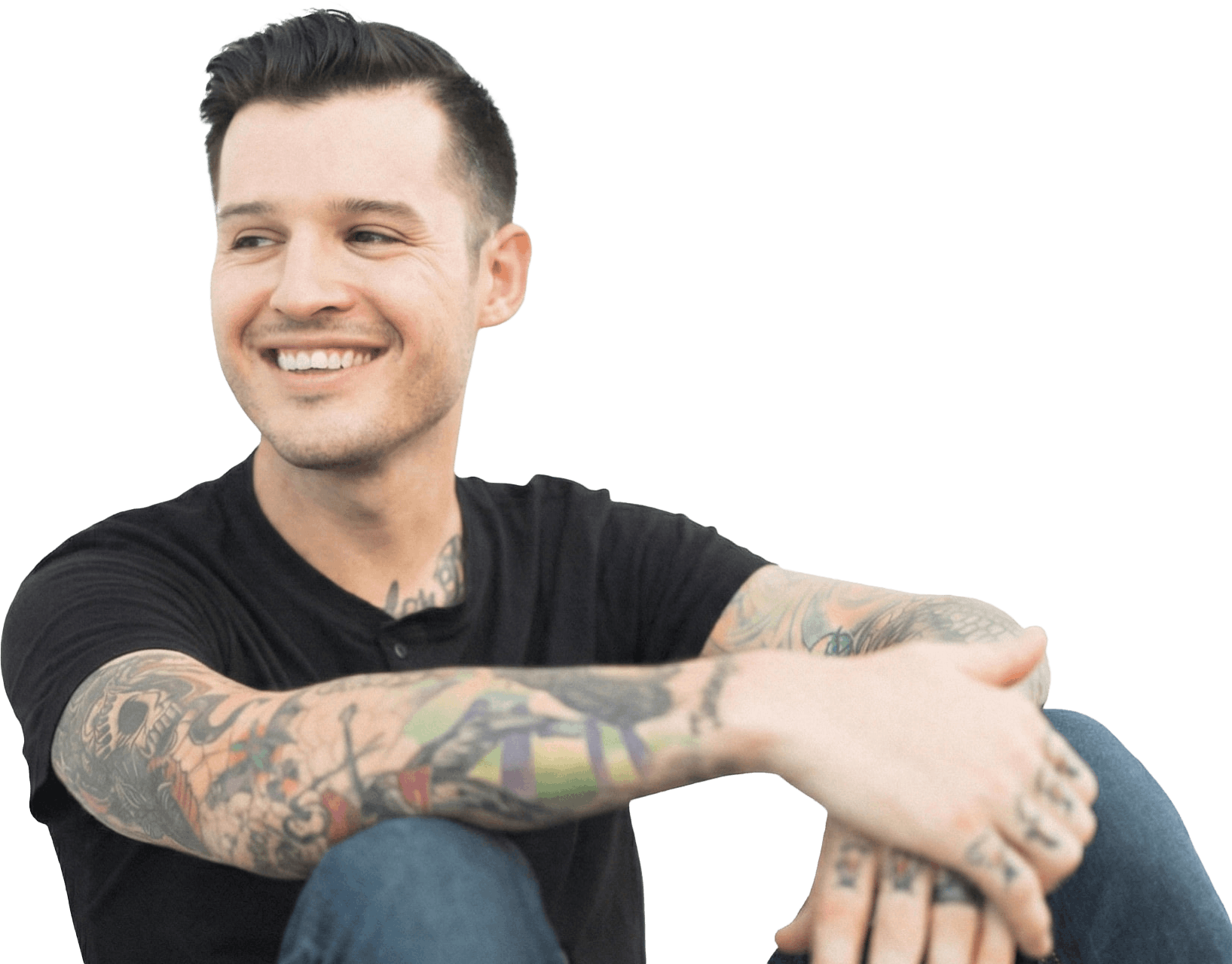 Homme assis décontracté souriant regardant vers la gauche avec tatouages, jeans et T-shirt gris foncé